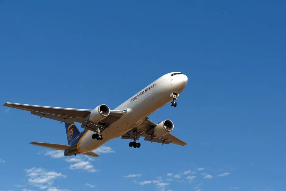 A cargo plane from a well-known logistics company flies against a vibrant blue sky.