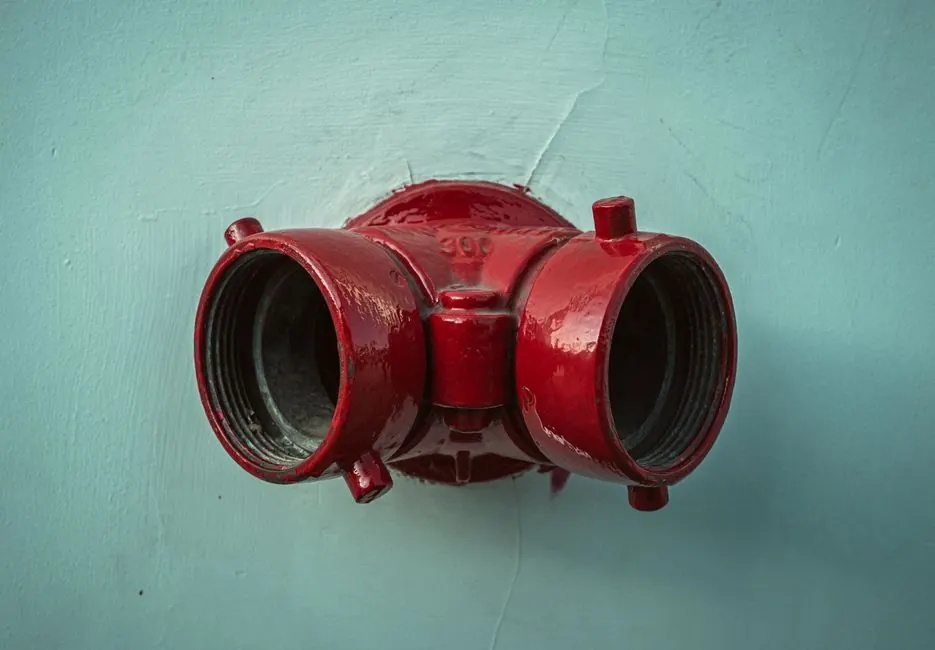 A vibrant red fire hydrant contrasts against a light blue wall, showcasing urban infrastructure.